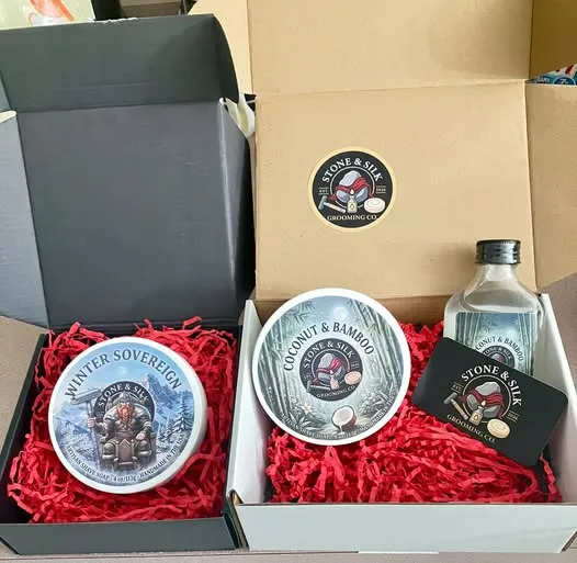 Product photography of Stone & Silk Grooming Co. shaving soap tubs, showing the brand's packaging and label artwork for its Coconut & Bamboo and Winter Sovereign scents.
