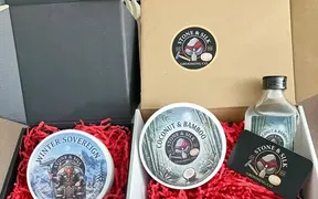 Product photography of Stone & Silk Grooming Co. shaving soap tubs, showing the brand's packaging and label artwork for its Coconut & Bamboo and Winter Sovereign scents.