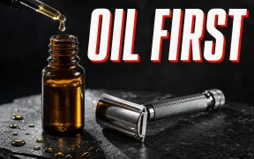 A dramatic side-lit photograph on dark slate of an amber glass bottle of pre-shave oil with a dropper cap, a golden drop of oil suspended at the dropper tip, a chrome double-edge safety razor lying beside it, headline OIL FIRST in white block letters with a red drop shadow across the top