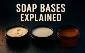 Advertisement style hero of three open shaving soap tubs on wet dark slate, a swirled ivory tallow soap, a smooth pale vegan soap, and a glassy amber glycerin soap, under the headline SOAP BASES EXPLAINED