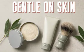 A calm flatlay on a pale bone-colored surface of a shaving soap puck, a tube of shaving cream, and a badger brush with soft even light, a small green leaf motif suggesting gentleness, headline GENTLE ON SKIN in white block letters with a soft red drop shadow across the top