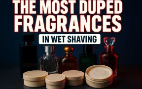 A dramatic flat lay of unlabeled luxury fragrance bottles standing behind a row of shaving soap tubs on dark slate, headline THE MOST DUPED FRAGRANCES in huge white block letters with a red drop shadow and IN WET SHAVING beneath it