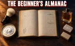 An old cloth-bound almanac lies open on a dark walnut counter, its pages ruled into columns of figures with small drawings of a sun dial, moon phases, a sprig of herbs and a star chart. Around it sit a shaving brush with a bone-white knot and a dark wooden handle, an open tin of shave soap topped with a swirl of white lather, a translucent alum block, a plain brown carton of razor blades and a square glass bottle of amber aftershave. Headline THE BEGINNER'S ALMANAC in white block capitals with a red drop shadow across the top.