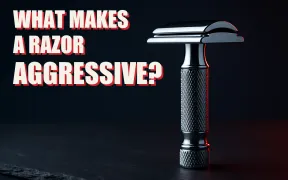 A chrome double edge safety razor standing upright on dark slate, its closed comb head shown in profile with the blade seam visible between cap and safety bar, beside the headline WHAT MAKES A RAZOR AGGRESSIVE in white block letters with a red drop shadow