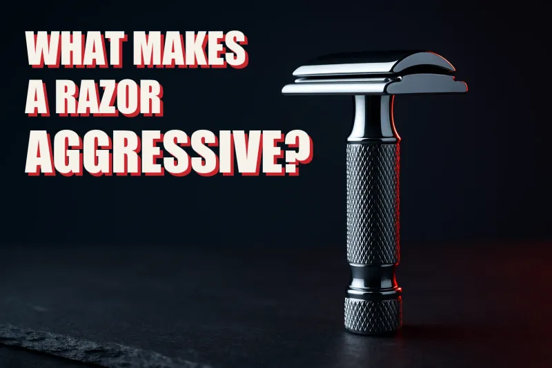 A chrome double edge safety razor standing upright on dark slate, its closed comb head shown in profile with the blade seam visible between cap and safety bar, beside the headline WHAT MAKES A RAZOR AGGRESSIVE in white block letters with a red drop shadow