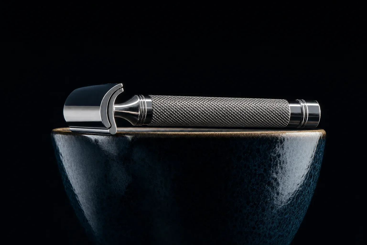 A safety razor resting level and untouched across the rim of a ceramic lather bowl against a dark background, showing its own weight is enough.